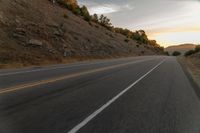 a motorcycle driving on a empty highway towards the horizon with hills in the background and a cloudy sky