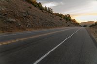 a motorcycle driving on a empty highway towards the horizon with hills in the background and a cloudy sky