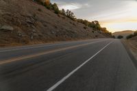 a motorcycle driving on a empty highway towards the horizon with hills in the background and a cloudy sky