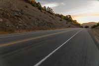 a motorcycle driving on a empty highway towards the horizon with hills in the background and a cloudy sky