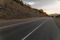 a motorcycle driving on a empty highway towards the horizon with hills in the background and a cloudy sky