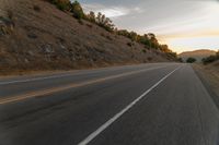 a motorcycle driving on a empty highway towards the horizon with hills in the background and a cloudy sky