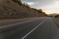 a motorcycle driving on a empty highway towards the horizon with hills in the background and a cloudy sky