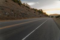 a motorcycle driving on a empty highway towards the horizon with hills in the background and a cloudy sky