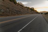 a motorcycle driving on a empty highway towards the horizon with hills in the background and a cloudy sky