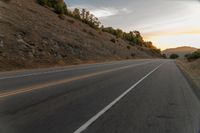 a motorcycle driving on a empty highway towards the horizon with hills in the background and a cloudy sky