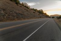 a motorcycle driving on a empty highway towards the horizon with hills in the background and a cloudy sky