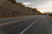 a motorcycle driving on a empty highway towards the horizon with hills in the background and a cloudy sky