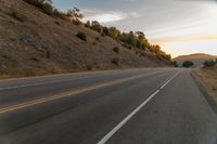 a motorcycle driving on a empty highway towards the horizon with hills in the background and a cloudy sky