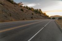 a motorcycle driving on a empty highway towards the horizon with hills in the background and a cloudy sky