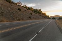 a motorcycle driving on a empty highway towards the horizon with hills in the background and a cloudy sky