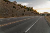 a motorcycle driving on a empty highway towards the horizon with hills in the background and a cloudy sky