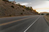 a motorcycle driving on a empty highway towards the horizon with hills in the background and a cloudy sky