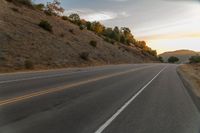 a motorcycle driving on a empty highway towards the horizon with hills in the background and a cloudy sky