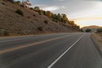 a motorcycle driving on a empty highway towards the horizon with hills in the background and a cloudy sky