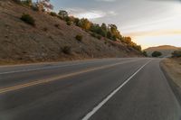 a motorcycle driving on a empty highway towards the horizon with hills in the background and a cloudy sky