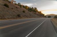 a motorcycle driving on a empty highway towards the horizon with hills in the background and a cloudy sky