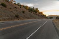 a motorcycle driving on a empty highway towards the horizon with hills in the background and a cloudy sky