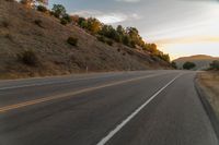 a motorcycle driving on a empty highway towards the horizon with hills in the background and a cloudy sky