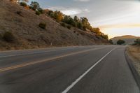 a motorcycle driving on a empty highway towards the horizon with hills in the background and a cloudy sky