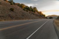 a motorcycle driving on a empty highway towards the horizon with hills in the background and a cloudy sky