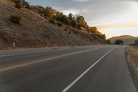 a motorcycle driving on a empty highway towards the horizon with hills in the background and a cloudy sky