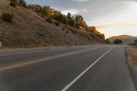 a motorcycle driving on a empty highway towards the horizon with hills in the background and a cloudy sky