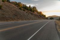 a motorcycle driving on a empty highway towards the horizon with hills in the background and a cloudy sky