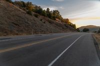 a motorcycle driving on a empty highway towards the horizon with hills in the background and a cloudy sky