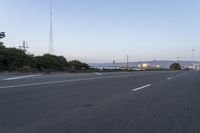 an empty highway at dusk with mountains in the background and lights on as traffic passes