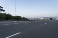 an empty highway at dusk with mountains in the background and lights on as traffic passes