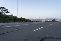 an empty highway at dusk with mountains in the background and lights on as traffic passes