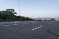 an empty highway at dusk with mountains in the background and lights on as traffic passes