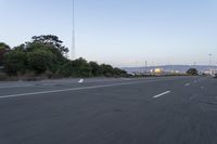 an empty highway at dusk with mountains in the background and lights on as traffic passes