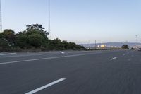 an empty highway at dusk with mountains in the background and lights on as traffic passes