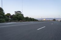 an empty highway at dusk with mountains in the background and lights on as traffic passes