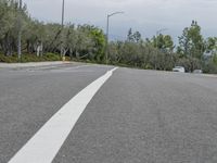 car driving on empty highway through forest and hills with traffic lights above it, with a white truck at its stop light in distance