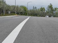 car driving on empty highway through forest and hills with traffic lights above it, with a white truck at its stop light in distance