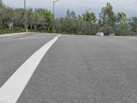 car driving on empty highway through forest and hills with traffic lights above it, with a white truck at its stop light in distance