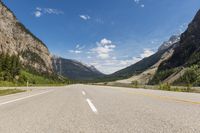 an empty highway leads into the mountains in the canadian rockies of canada with yellow line ahead