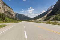 an empty highway leads into the mountains in the canadian rockies of canada with yellow line ahead