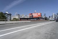 there is an empty highway with white stripes on it with a billboard above it and tall buildings in the distance