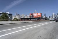 there is an empty highway with white stripes on it with a billboard above it and tall buildings in the distance