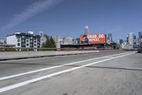 there is an empty highway with white stripes on it with a billboard above it and tall buildings in the distance