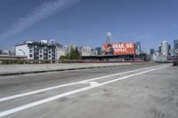 there is an empty highway with white stripes on it with a billboard above it and tall buildings in the distance