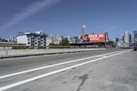 there is an empty highway with white stripes on it with a billboard above it and tall buildings in the distance