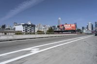 there is an empty highway with white stripes on it with a billboard above it and tall buildings in the distance