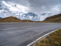 an empty highway with mountains in the background with clouds and snow on the mountain tops