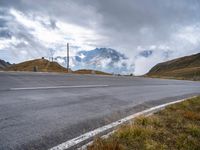 an empty highway with mountains in the background with clouds and snow on the mountain tops