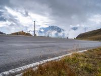 an empty highway with mountains in the background with clouds and snow on the mountain tops